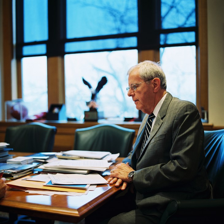 Mayor Ron Littlefield sitting at a desk with papers and documents in an office with large windows overlooking the city.