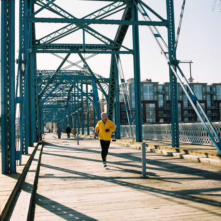 Runner in yellow jacket jogging across a teal steel bridge over the Tennessee River.