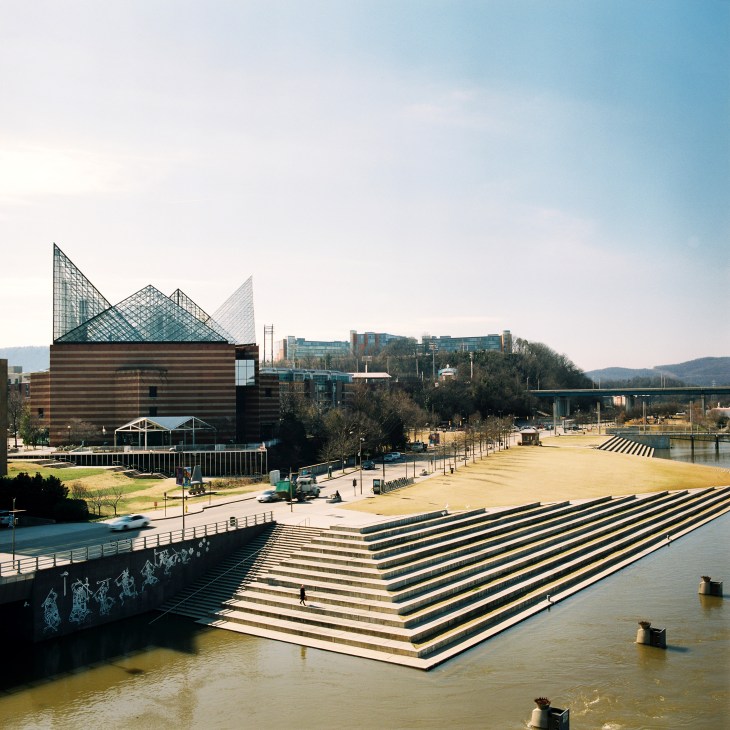 The Tennessee Aquarium building with geometric teal roofing beside the Tennessee River and stepped waterfront plaza.