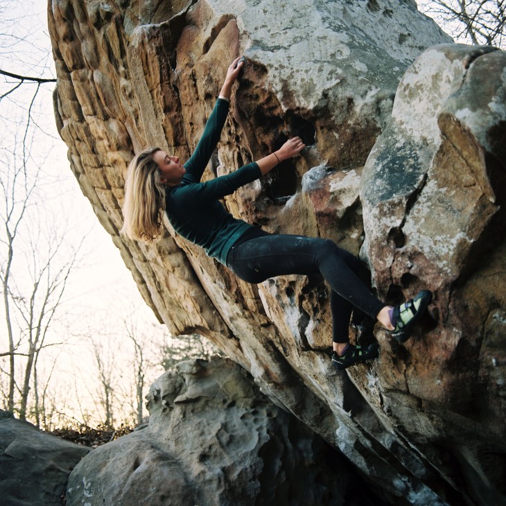 Woman rock climbing on a natural stone cliff face in an outdoor setting.