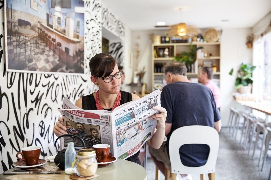 Woman reading The Sydney Morning Herald newspaper at a cafe table with coffee.