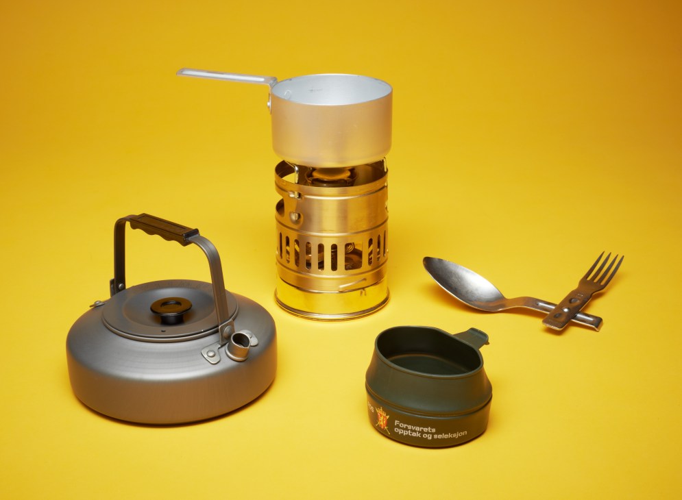 Nordic military mess kit including Optimus kettle and stove, Wildo cup, and Hackman cutlery on yellow background.