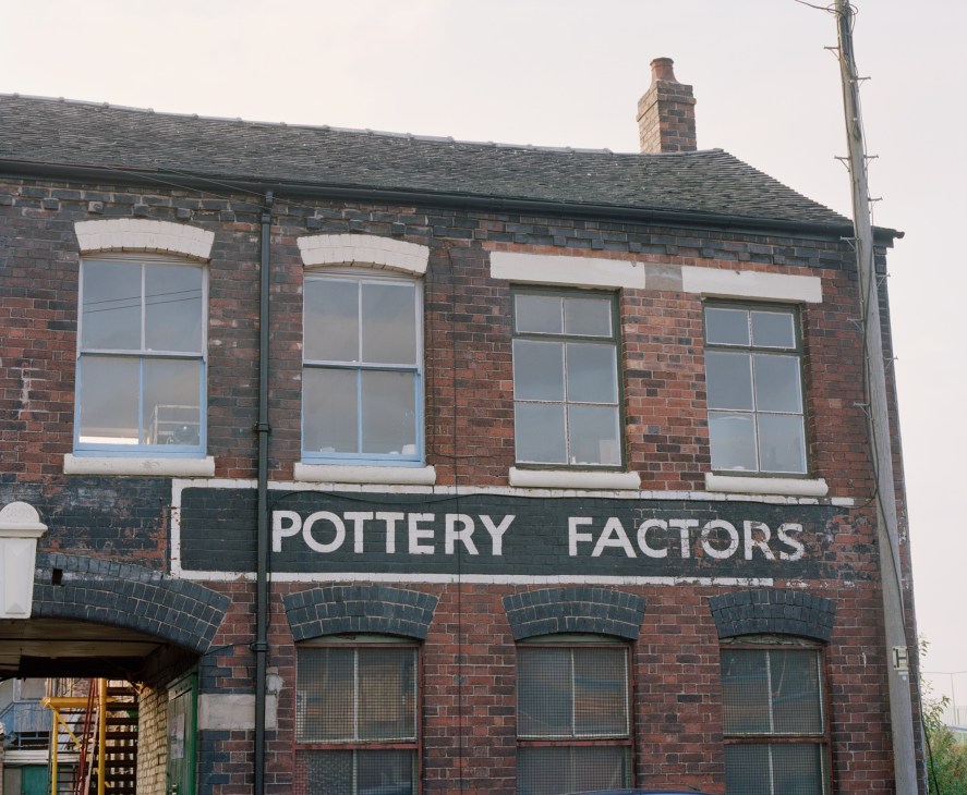 Red brick pottery factory building with white-trimmed windows and "POTTERY FACTORS" sign.