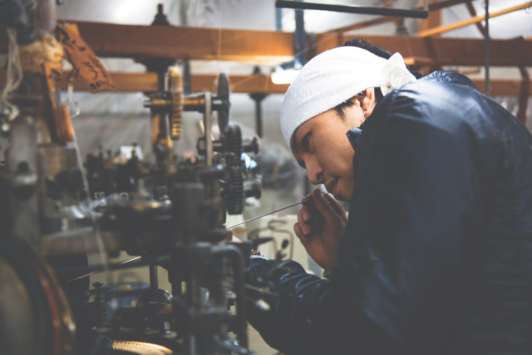 Factory technician Ryohei Kawasaki carefully removes dust from spinning gears of a loopwheel circular knitting machine.