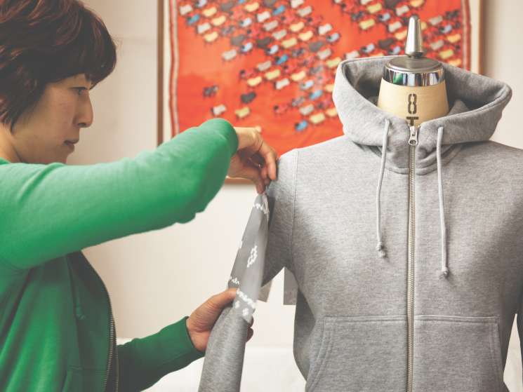 Pattern designer Fumiko Ishimoto adjusts a gray zip-up hoodie on a dress form.