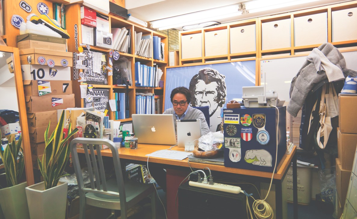Satoshi Suzuki works at his desk in a wooden-framed office above his Tokyo shop, surrounded by shelves of books and design references.