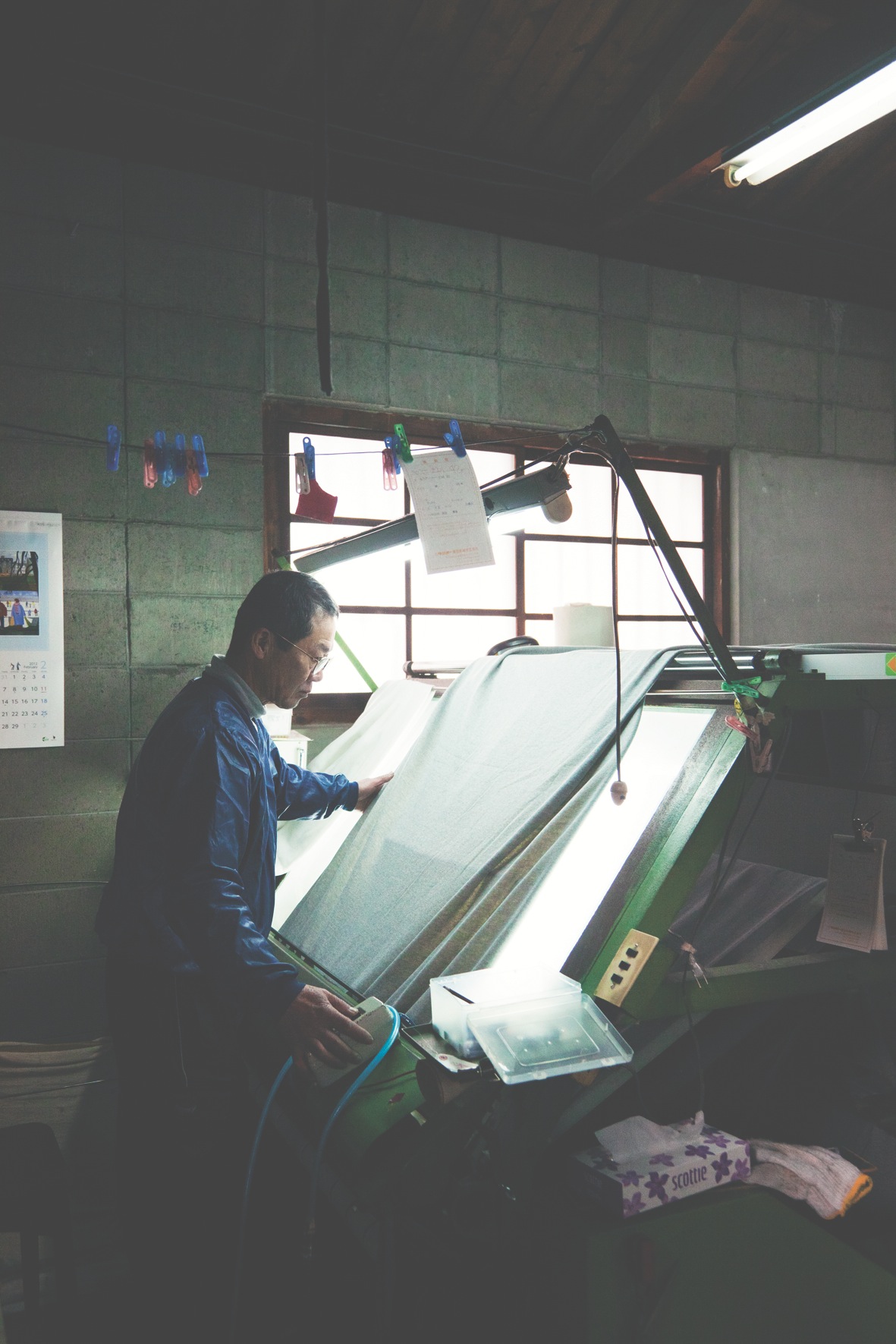 Factory worker inspects newly knitted cloth for quality at Kanekichi Industries.