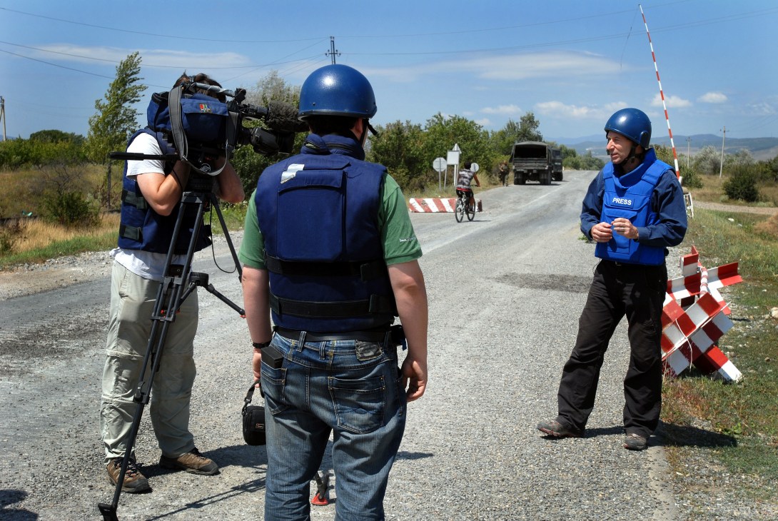BBC crew members wearing blue helmets and protective vests at a South Ossetian checkpoint on a rural road.