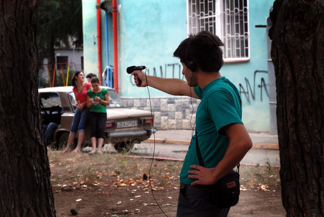 Soundman in teal shirt holding microphone and headphones during street recording in Georgia.