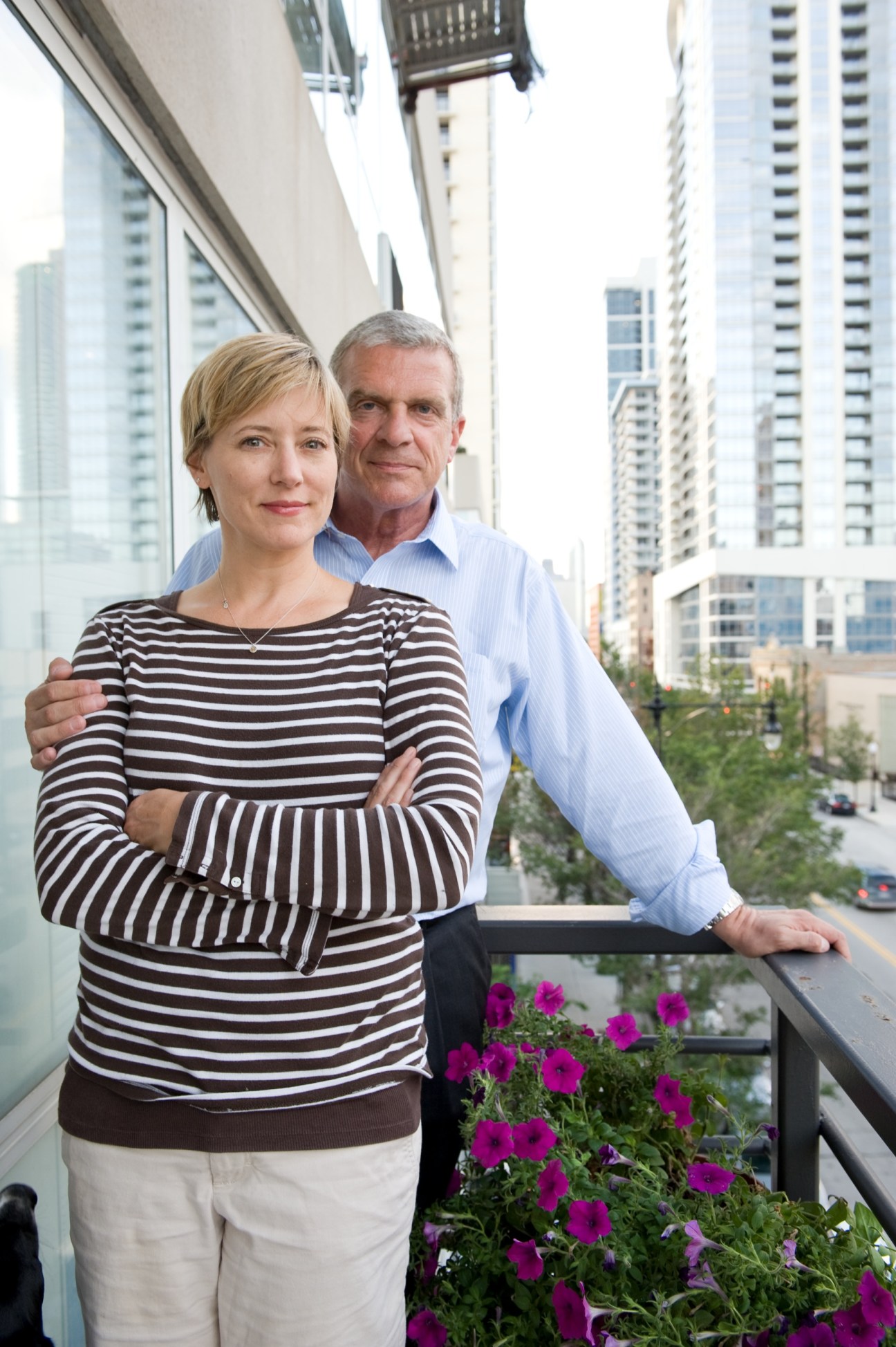 Christina Koening and Bill Buenger stand on a high-rise balcony overlooking Chicago's downtown skyline with purple flowers.