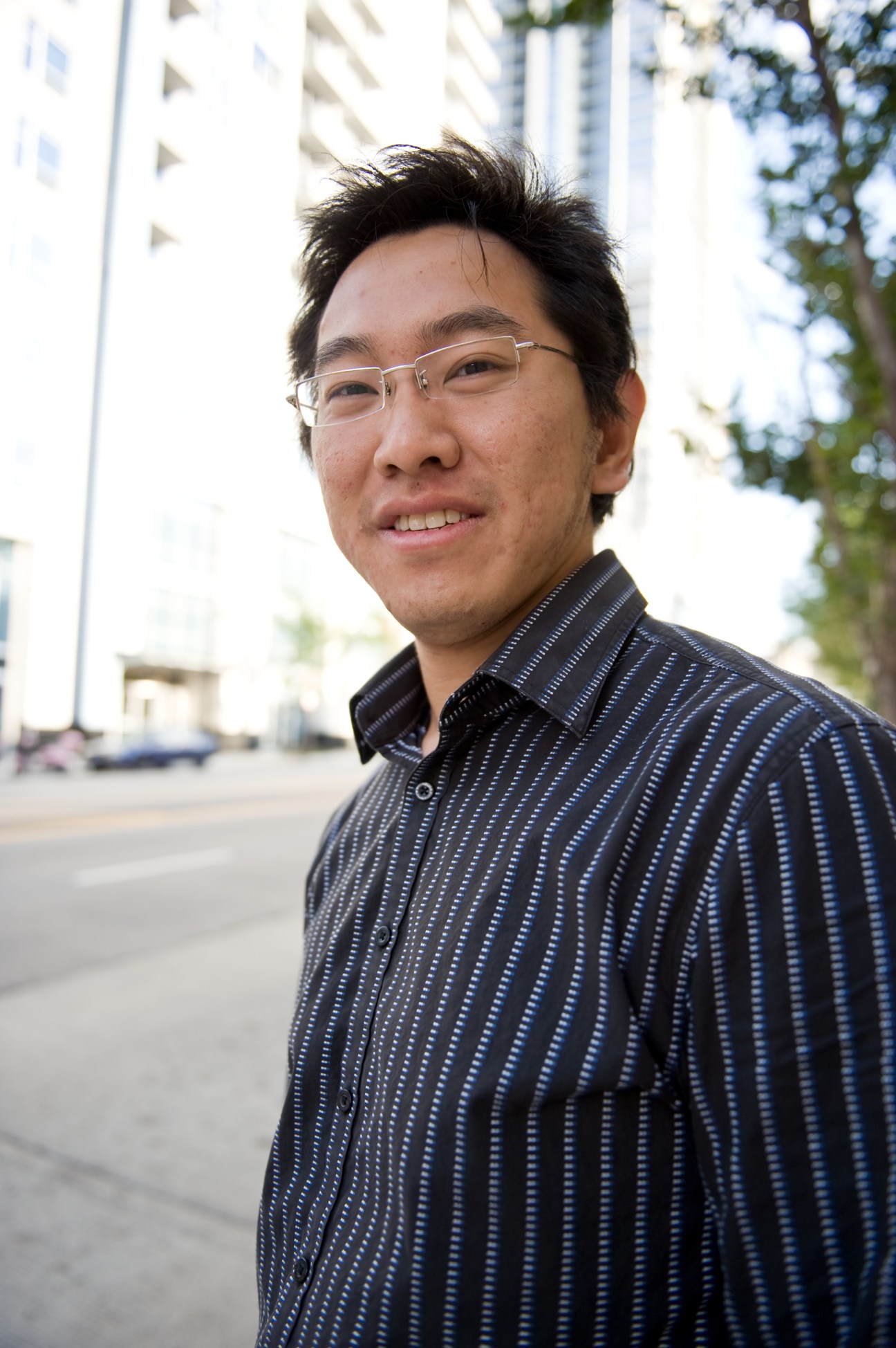Tao Xu, a law student, smiles at the camera wearing glasses and a striped shirt in front of modern buildings in South Loop Chicago.