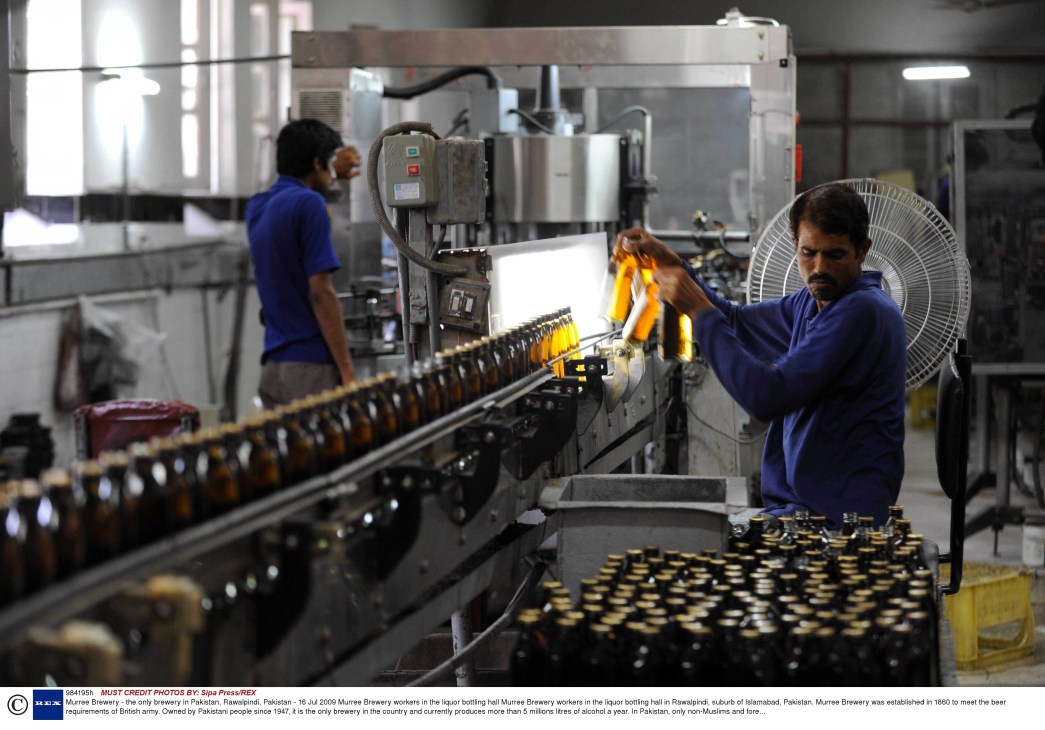 Workers in blue uniforms operate a beer bottling line at Murree Brewery in Pakistan.
