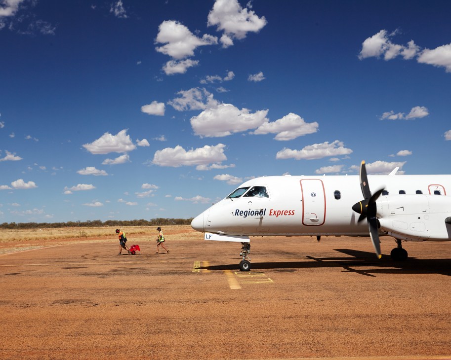Regional Express Saab 340 aircraft parked on red dirt runway at Windorah Airport under blue sky with white clouds.