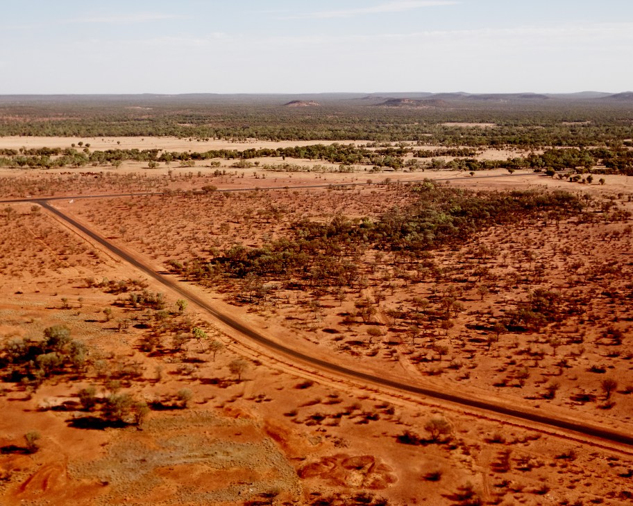 Aerial view of arid outback landscape in western Queensland with sparse vegetation and a dirt road.