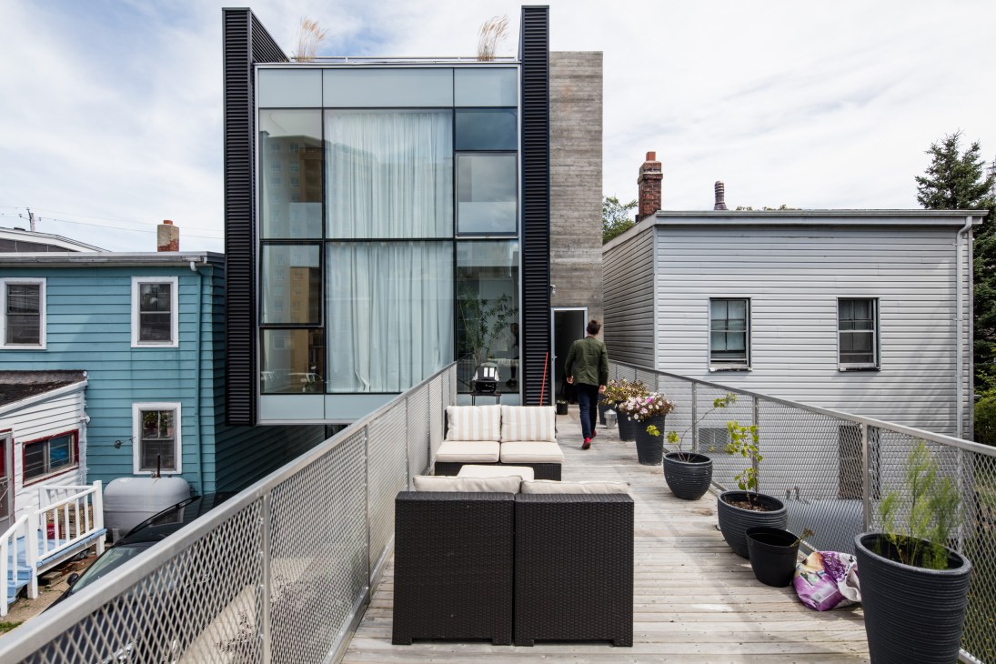 Modern glass and steel home with rooftop deck overlooking colorful neighborhood houses
