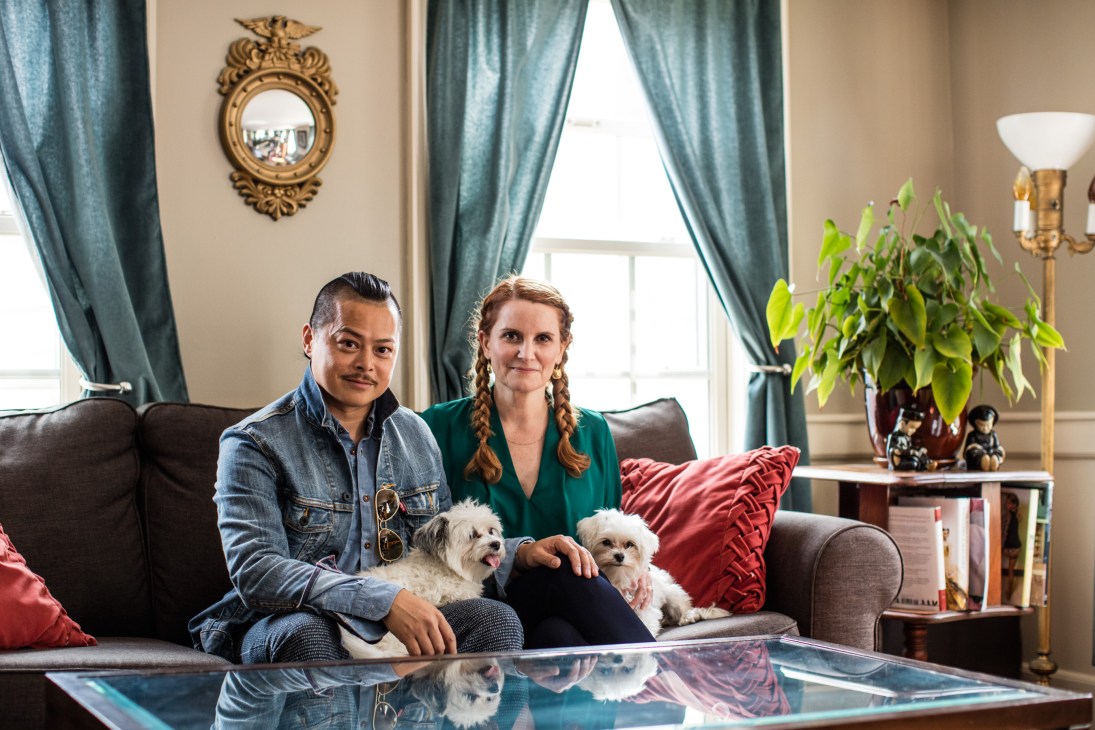 Benjamin Fong and Wendy Friedman sitting on a grey sofa with two small white dogs in an elegant living room