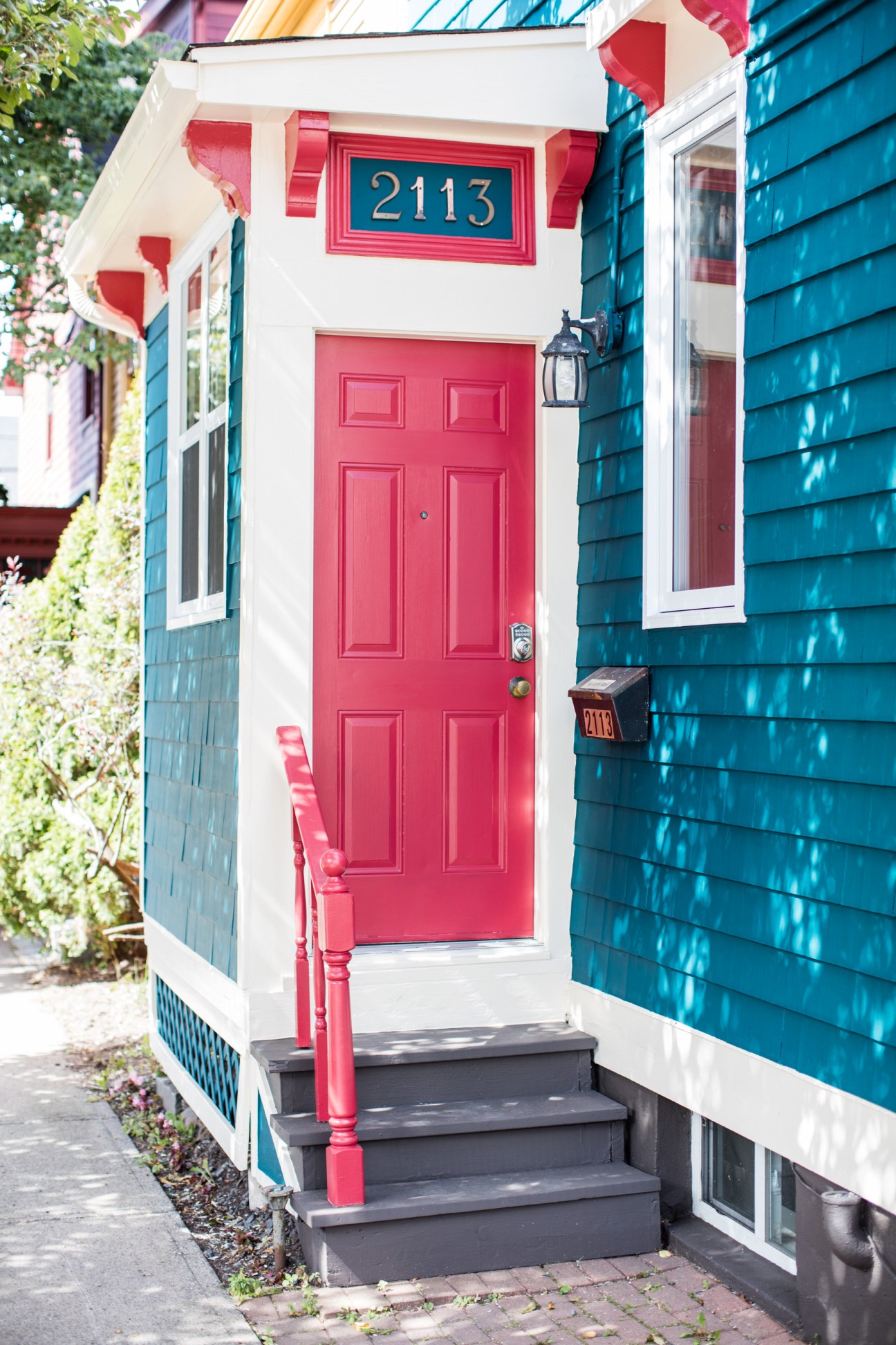 Colorful house entrance with red door, white trim, and blue shingle siding showing house number 2113
