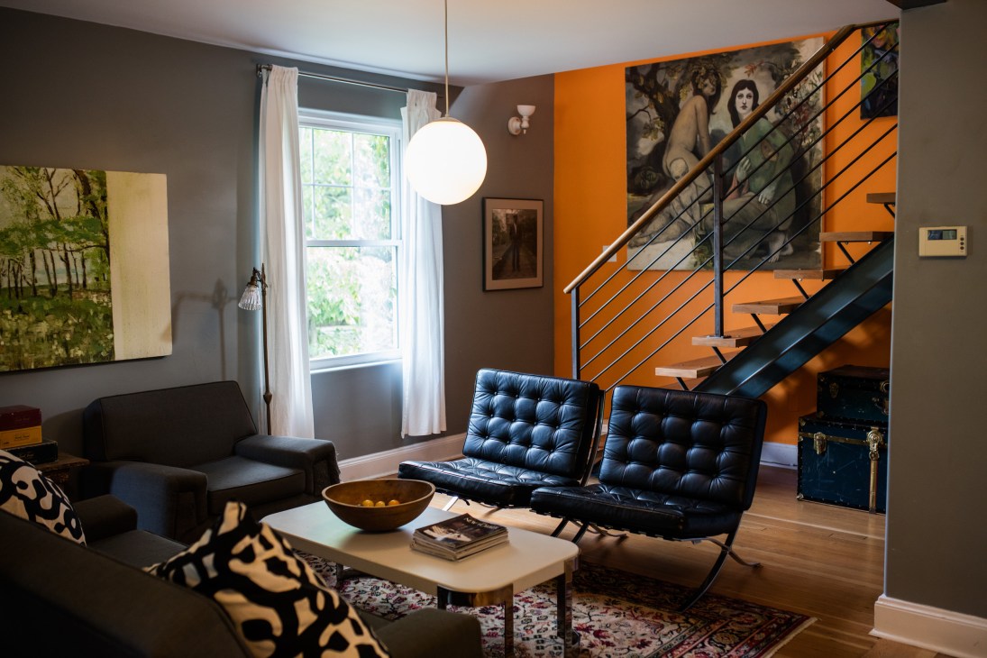 Modern living room with black leather chairs, orange accent wall, and metal staircase in Lezlie Lowe's home