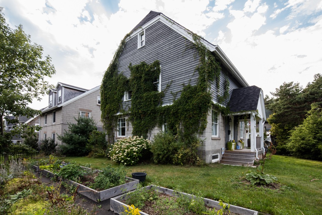 Ivy-covered house with wooden shingles and stone foundation surrounded by vegetable garden boxes