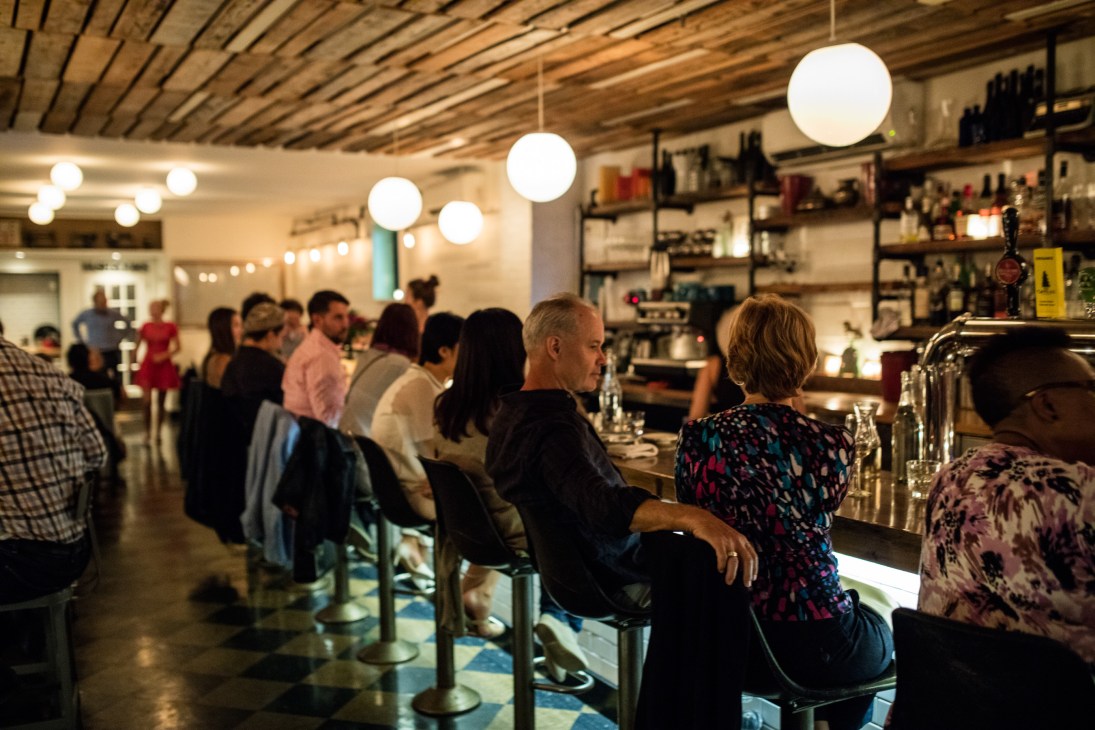 Diners seated at a bar in Edna seafood restaurant with pendant lights and exposed wooden ceiling