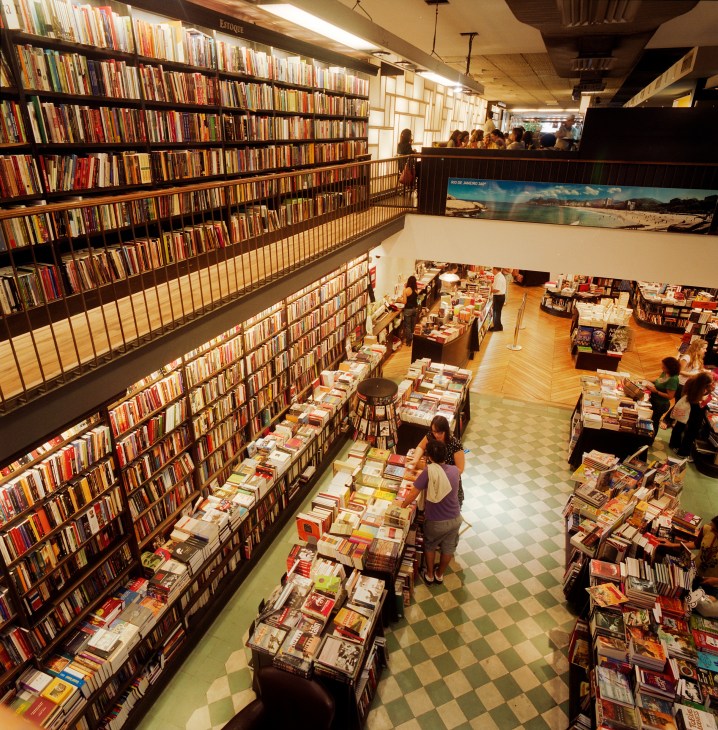 Interior of Livraria da Travessa bookstore showing multiple levels with floor-to-ceiling bookshelves and shoppers browsing.