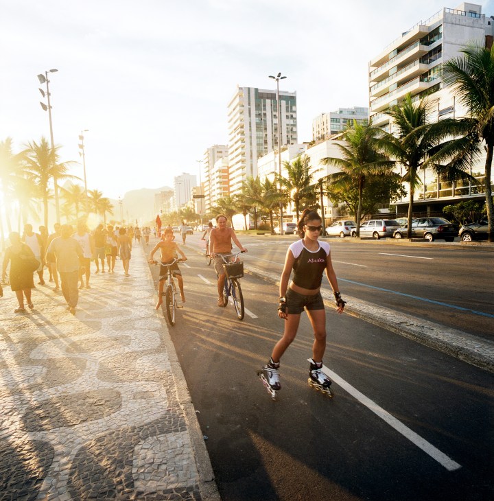 Woman rollerblading along Ipanema's beachfront promenade at golden hour with cyclists and pedestrians nearby.