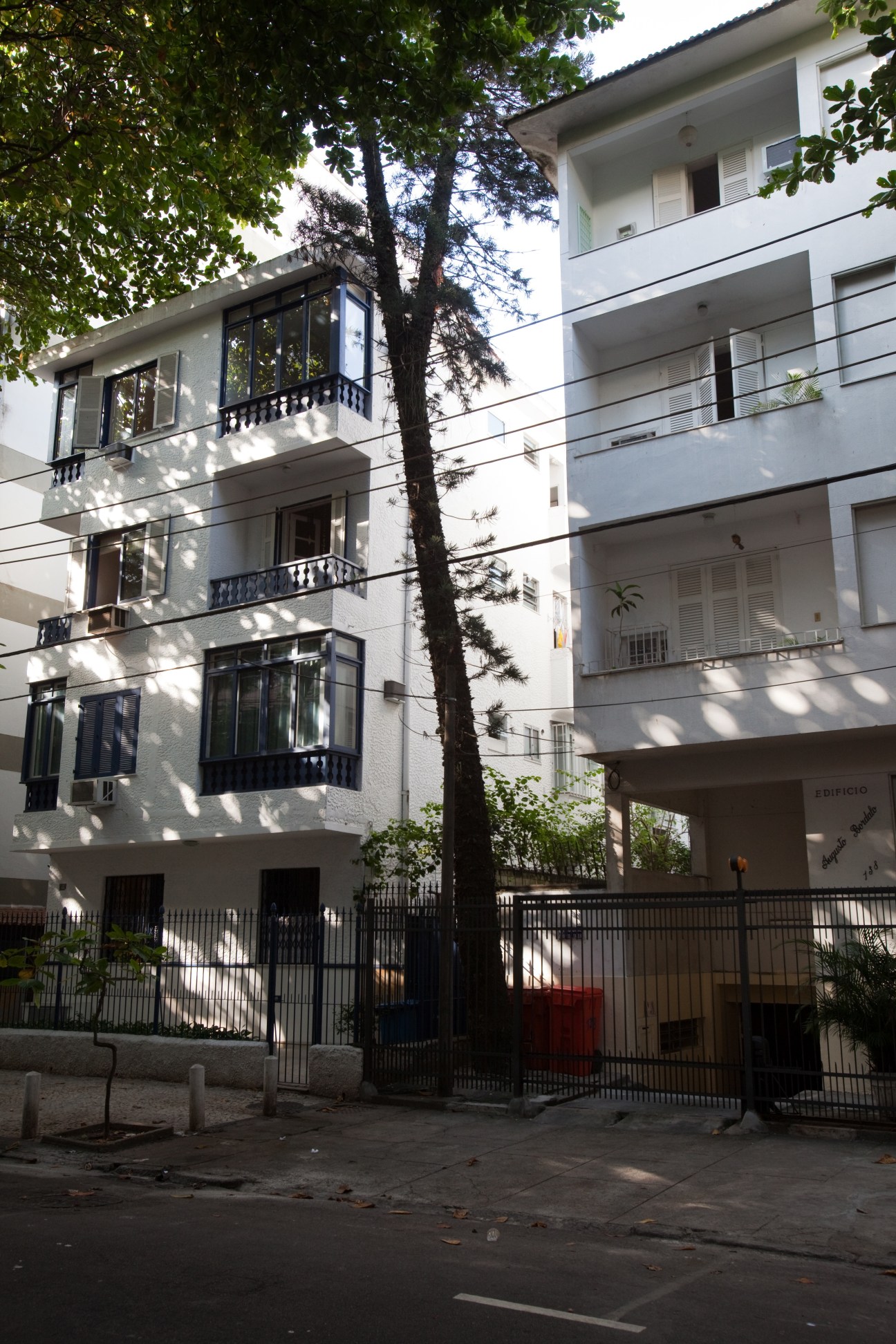 Modern white apartment building in Leblon with balconies and a tall tree in front.