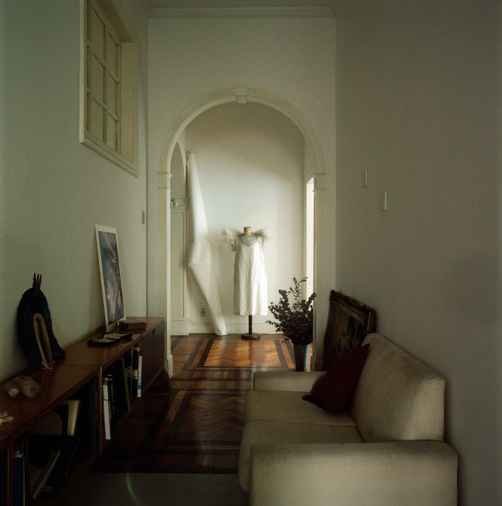Minimalist apartment interior with arched doorway, wooden furniture, and flowing white garment on dress form.