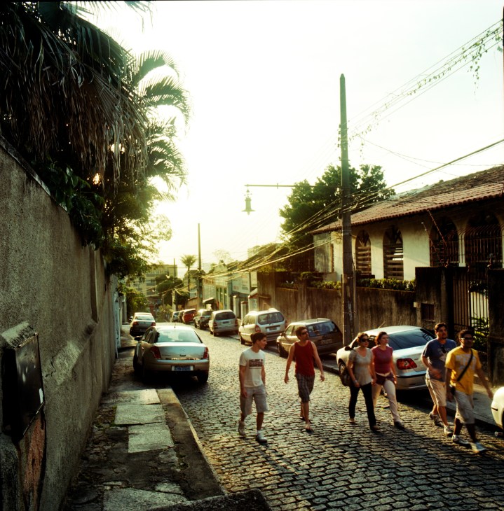 Cobblestone street in Santa Teresa with colonial buildings, palm trees, parked cars, and residents walking uphill.