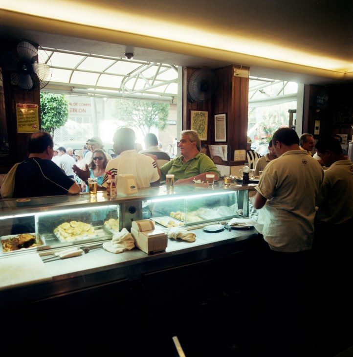 Interior of Bracarense bar in Leblon with customers seated at counter and illuminated display cases.