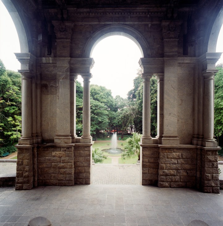 Stone archway entrance with columns framing a green garden and lush vegetation beyond.