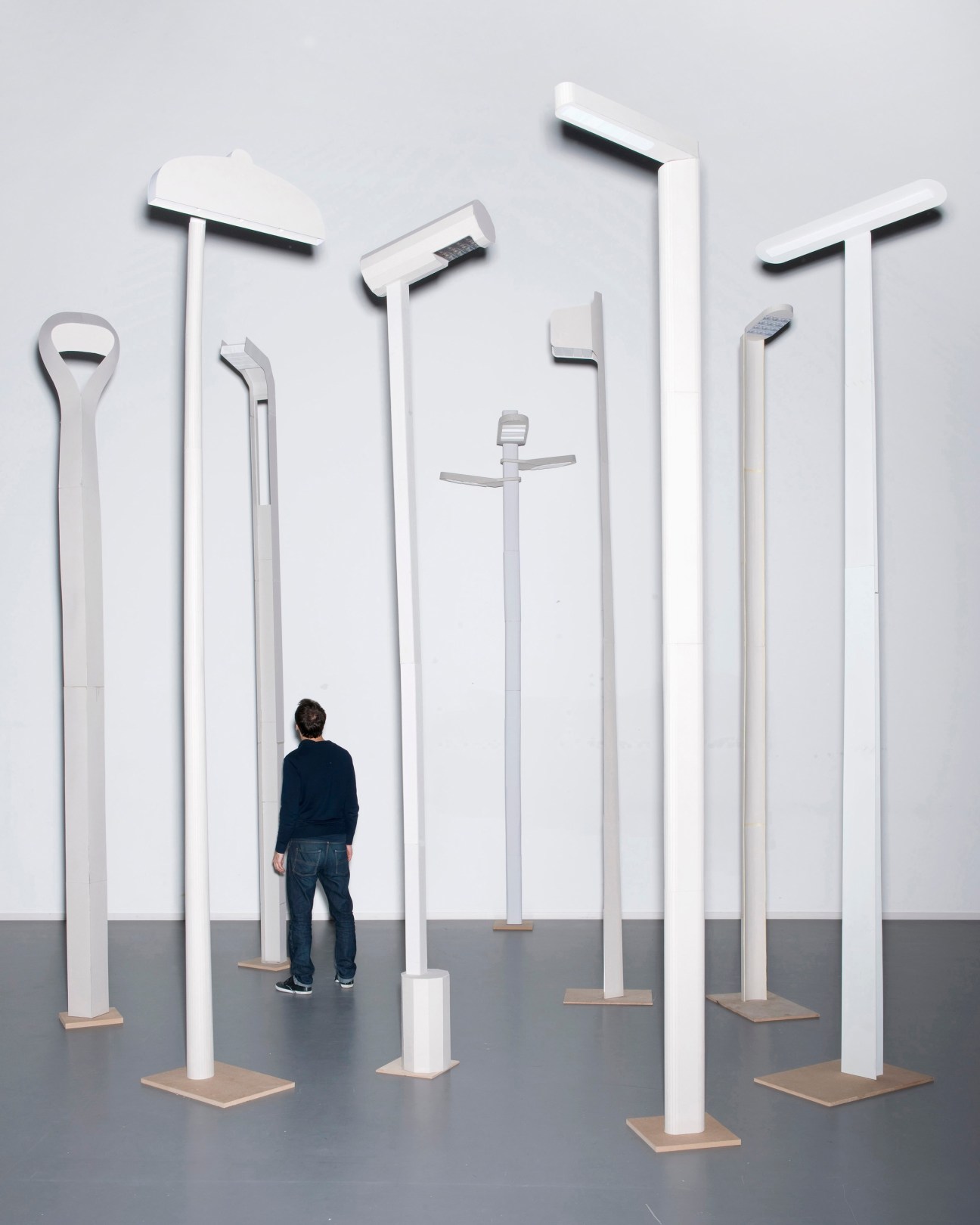 Display of various white and metal street lamps and lampposts with a person standing among them for scale.
