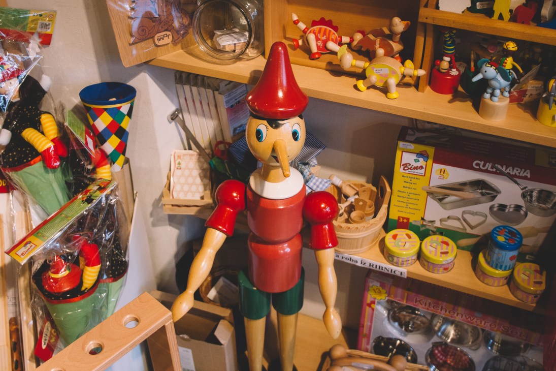Wooden Pinocchio puppet with red nose and clothing displayed among toys on shelves at Ristanc toy shop