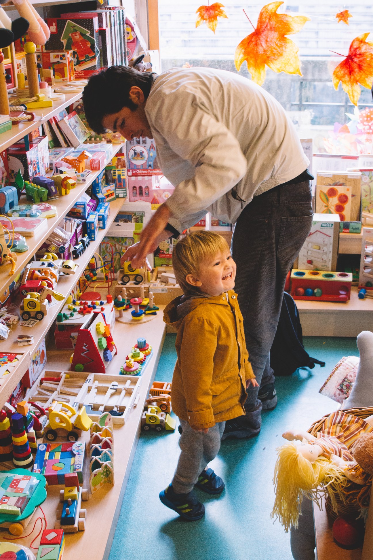 Adult and young child browsing toys at Ristanc shop with autumn leaf decorations.