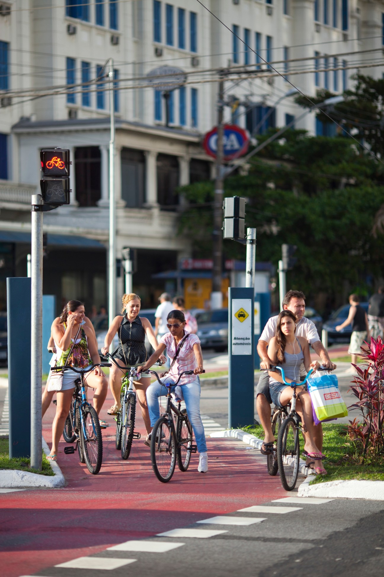People riding bicycles on a red bike lane along a beachside avenue in Santos with modern buildings in the background.
