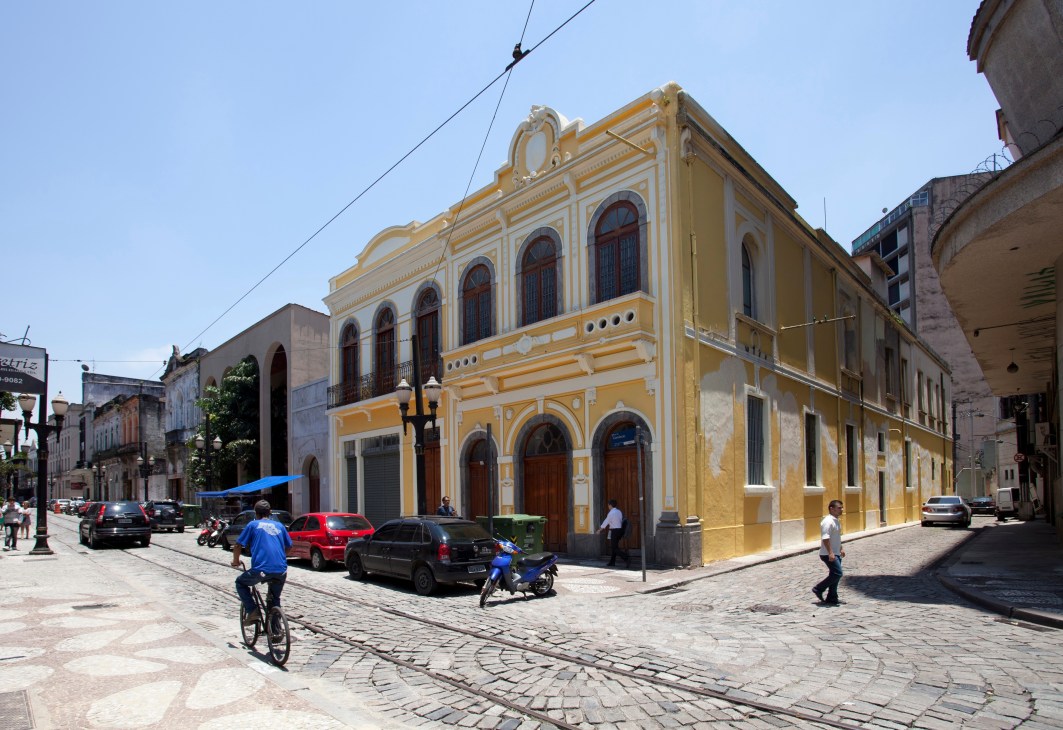 Yellow colonial building with arched windows in Santos historic centre square with pedestrians and parked cars