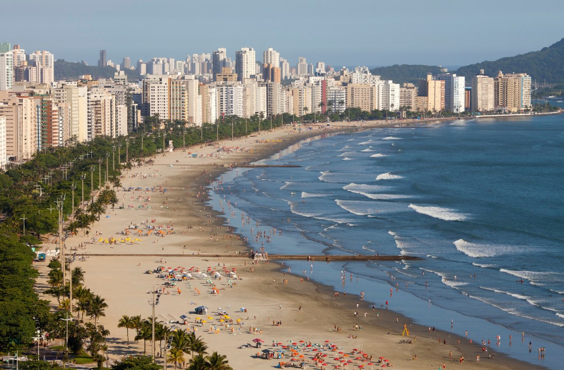 Santos beach with high-rise buildings, palm trees, and beachgoers along the sandy shore and ocean.