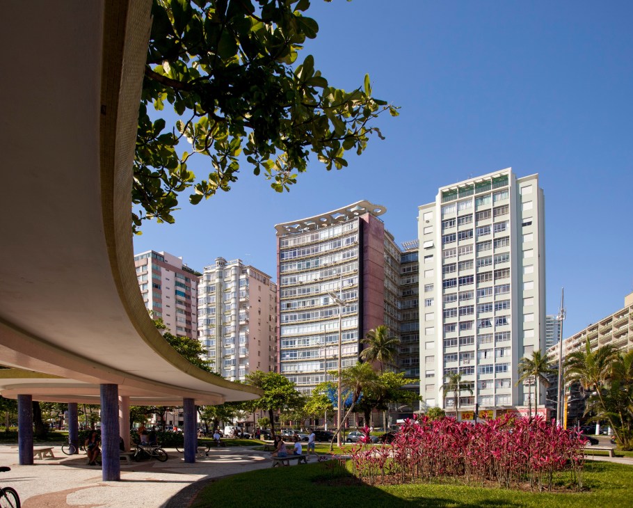 Modern apartment buildings and green space along Santos beachside promenade with palm trees and flowering plants.
