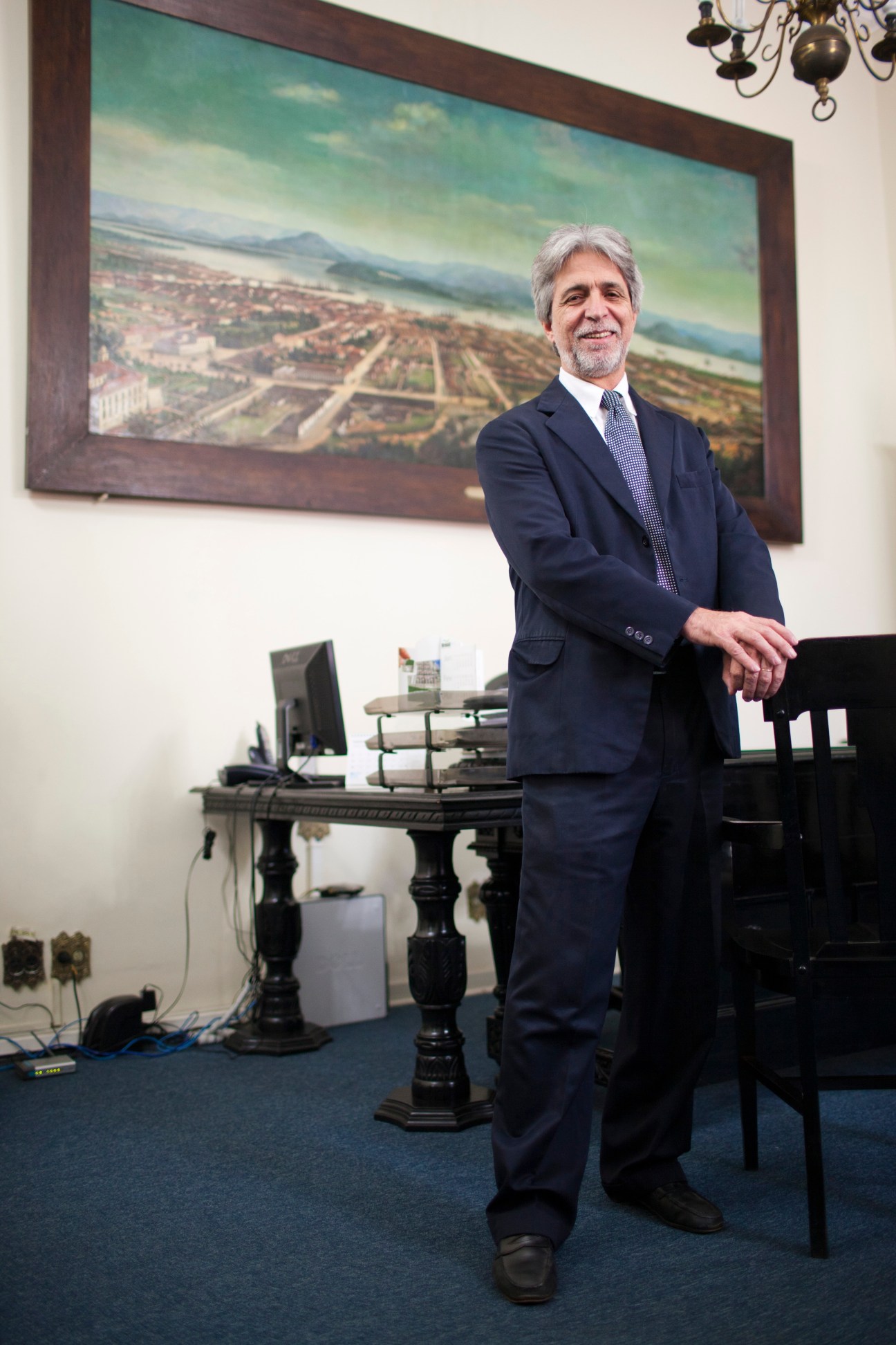 Marcio Calves, president of the Commercial Association, standing in an office with a framed landscape painting behind him.