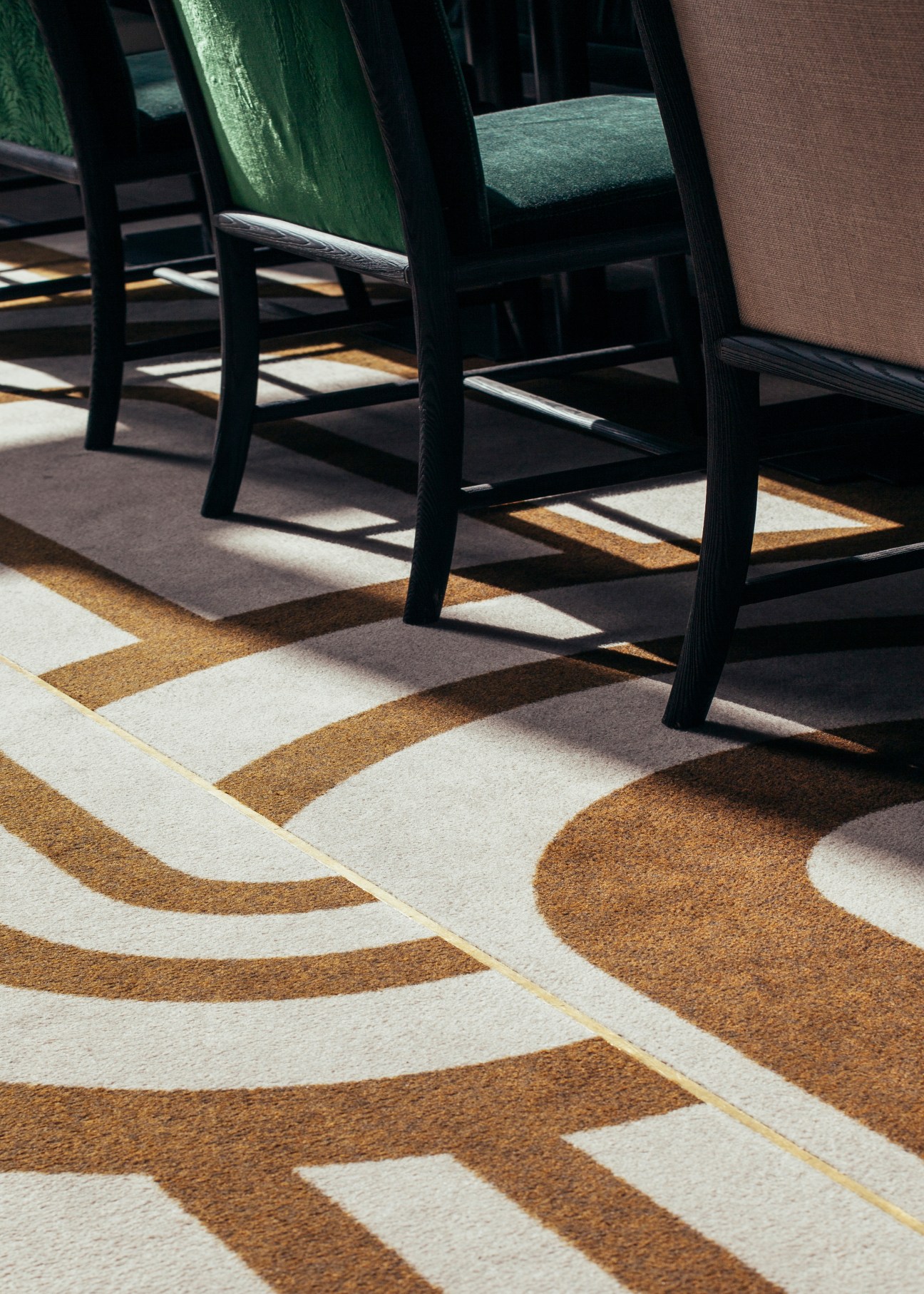 Black chairs with green and brown upholstery sit on a geometric patterned floor in cream, tan and brown tones.