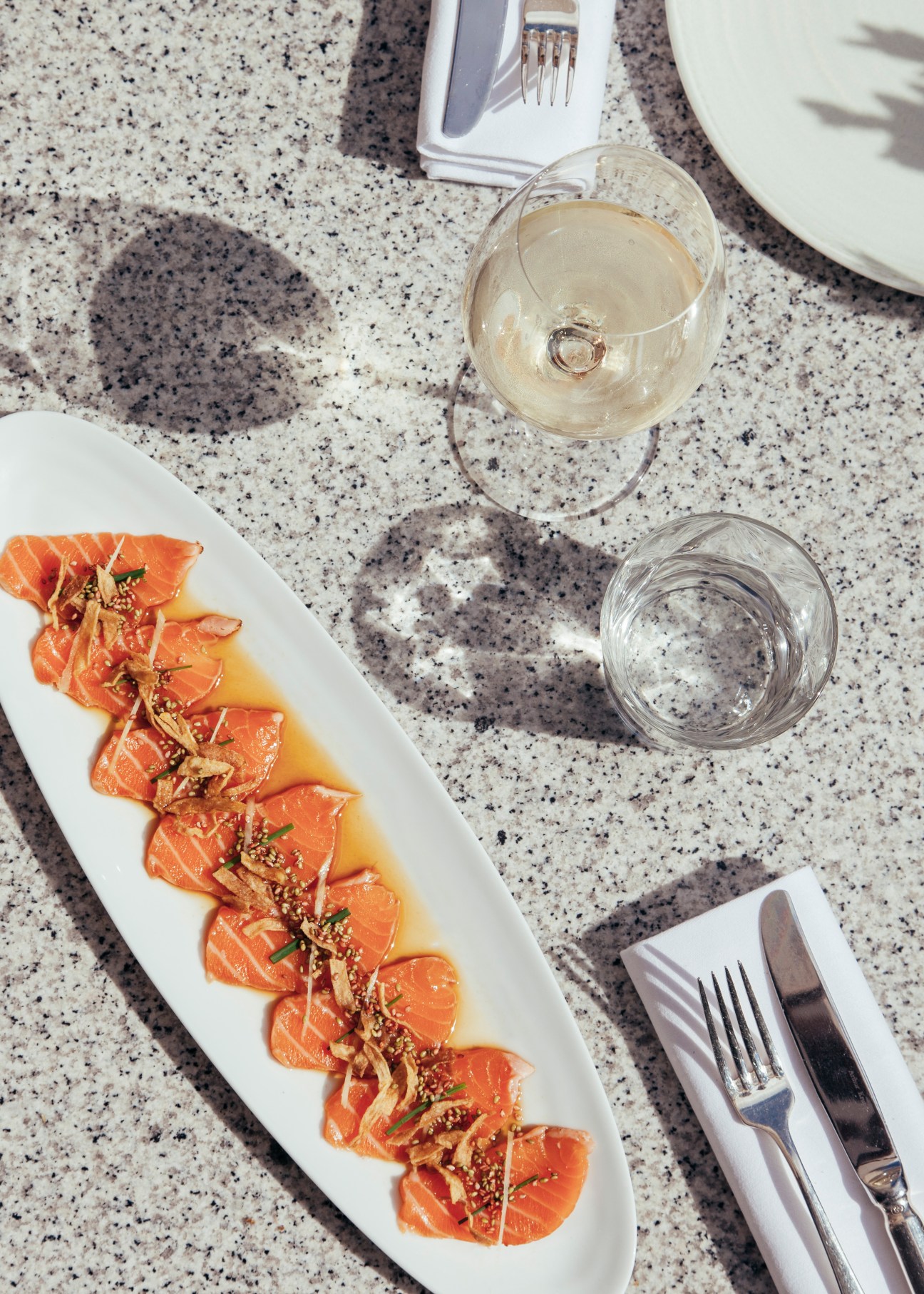 Salmon tataki with yuzu and wasabi served on a white plate with a speckled grey table setting.