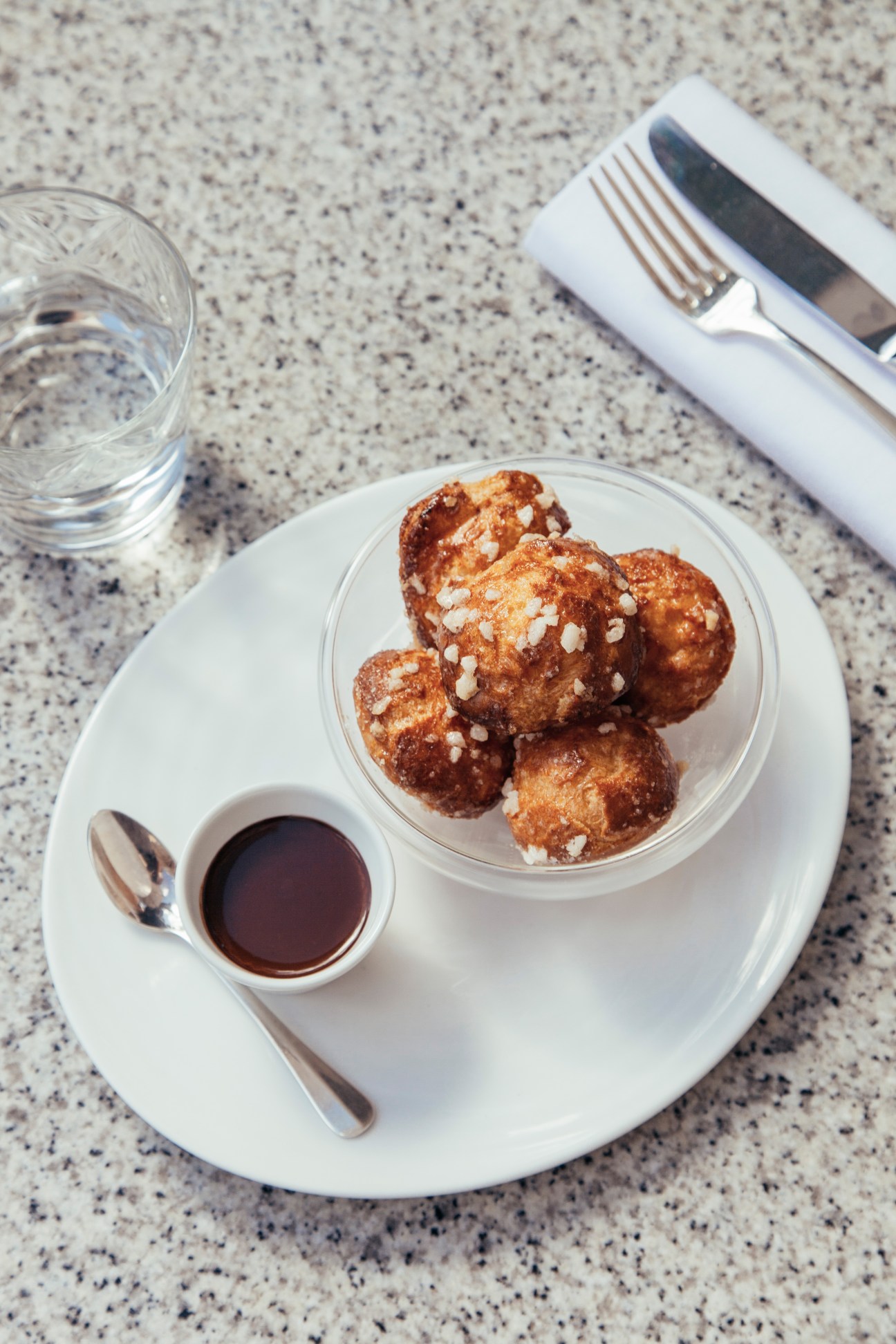 Cream-filled choux pastries topped with sea salt served with hot chocolate sauce on a speckled granite countertop.