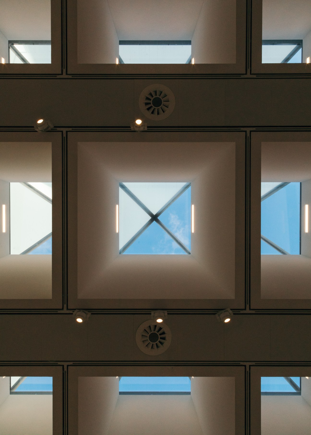 Pyramid-shaped glass rooflights with cross-bracing casting geometric shadows on concrete walls inside the renovated Hayward Gallery.
