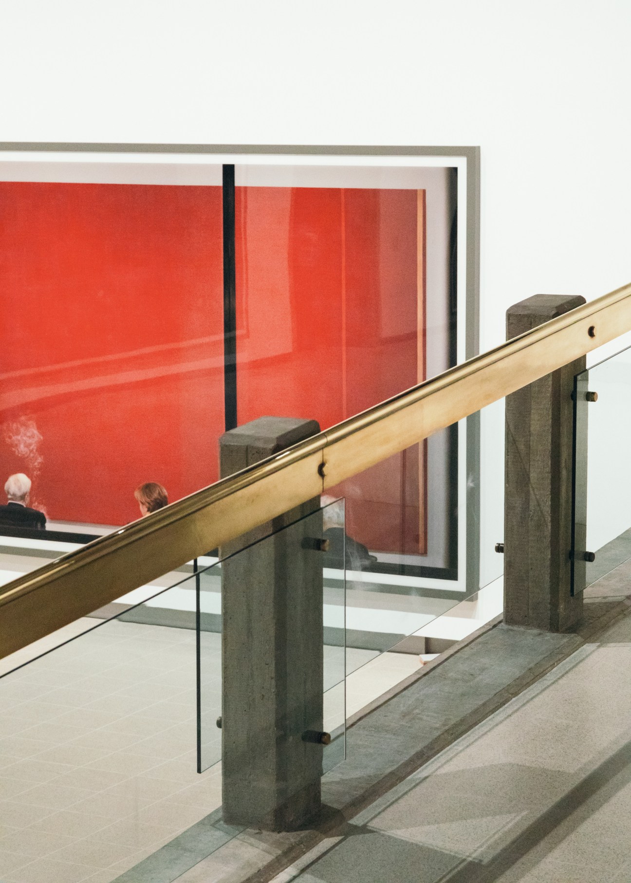 Polished brass handrail with concrete posts and glass balustrade overlooking Andreas Gursky's red artwork.