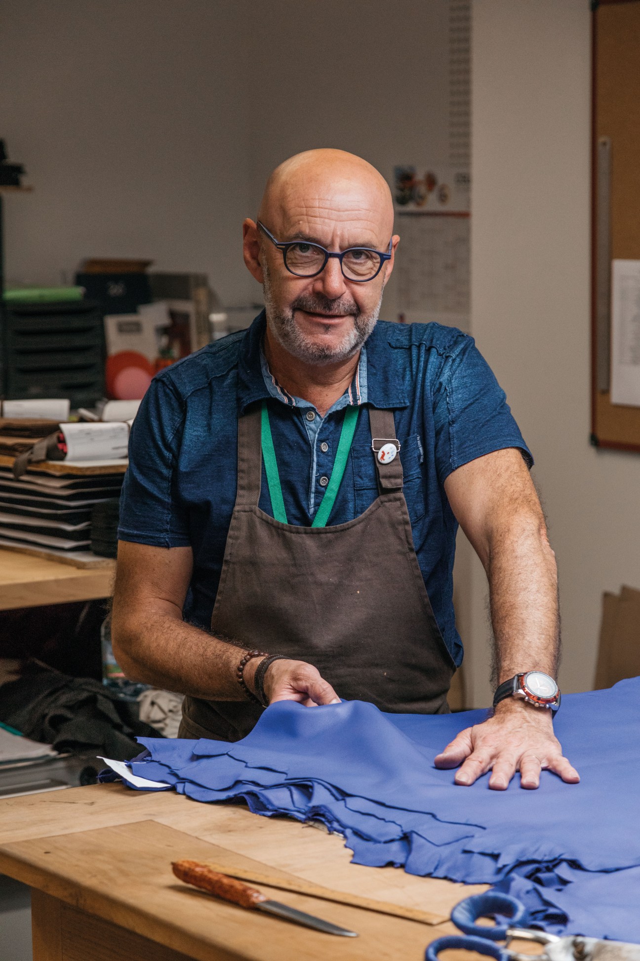 Jean-François Lefort, a 32-year glove-maker, stands at his workbench with blue leather gloves.