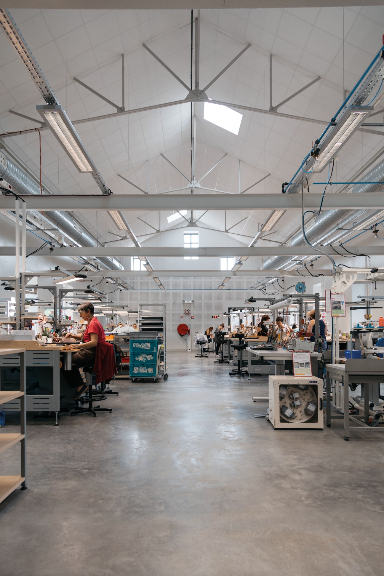 Interior of Hermès glove-making workshop in Saint-Junien with craftspeople working at wooden benches under industrial skylights.