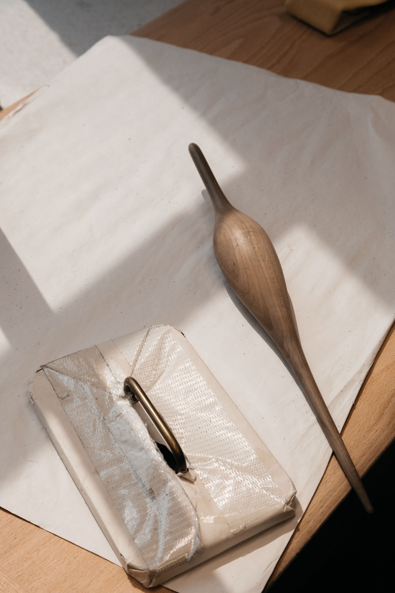Wooden glove-making tools including a main de fer template and wooden mallet on white paper and wooden surface.
