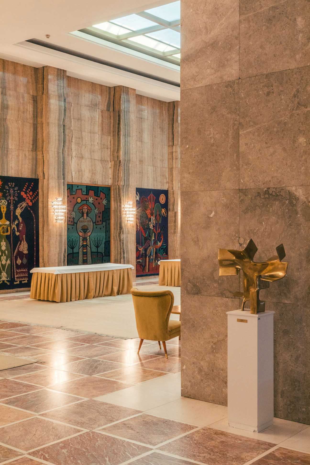 Mid-century modern lounge with golden chair, bronze sculpture, and colorful tapestries in Palace of Serbia