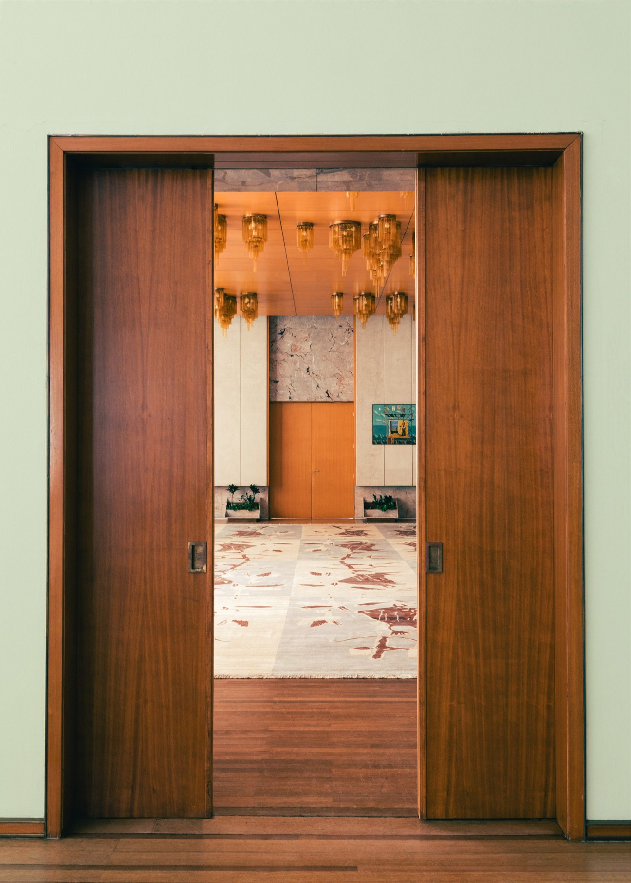 View through wooden doors into the Slovenian Salon with hanging brass fixtures and patterned marble flooring.
