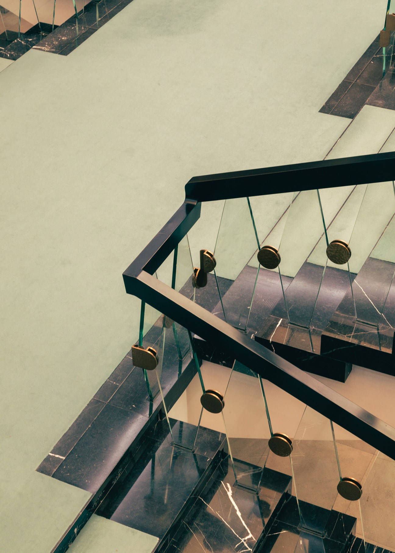 Overhead view of a modernist staircase with black railings and brass pendant light fixtures hanging from cables.